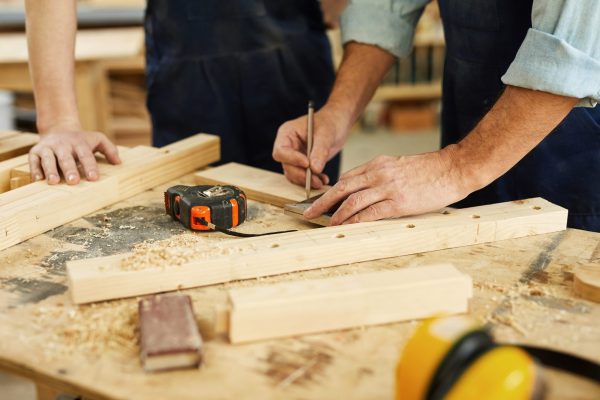 Close up of carpenters workstation with senior man measuring wood, copy space