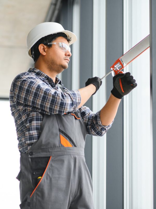 Workman in overalls installing or adjusting plastic windows.