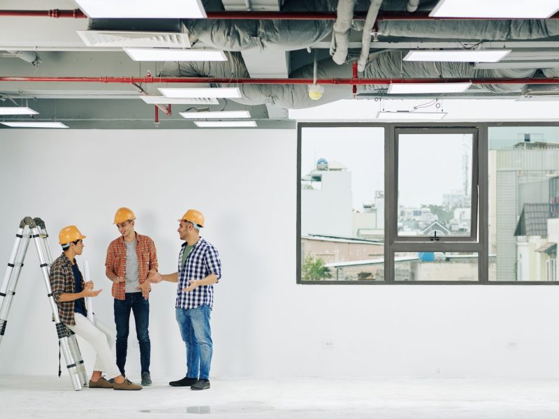 Young construction engineers in hard hats and plains shirts discussing news and gossips during short break at work